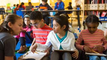 Elementary teacher discussing assignment with three students in media center
