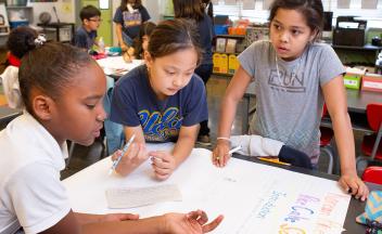 3 elementary students writing on flip chart in social studies unit