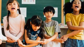 multicultural group of elementary kids holding hands in school