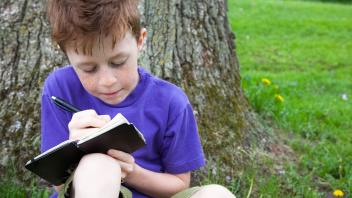 young red-headed boy outside writing in a notebook