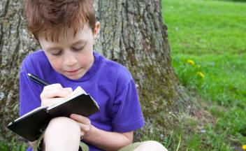 young red-headed boy outside writing in a notebook