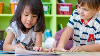 two elementary kids looking at a picture book in front of classroom library
