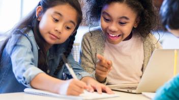 Two elementary students writing and talking in class