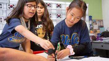 three elementary students making a list of words on flip chart paper