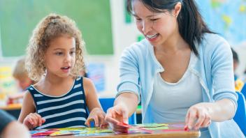 kindergarten teacher helping student with simple word cards