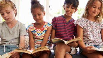 Four elementary aged kids sitting in a row and reading
