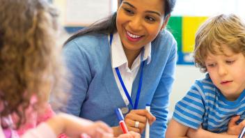Smiling elementary teacher helping two students with lesson
