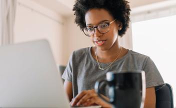 Young Black teacher looking at laptop at home