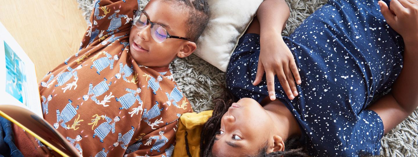 two kids lay on floor looking at an open picture book