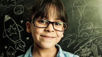 Young girl looking at camera with blackboard full of science chalk drawings behind her