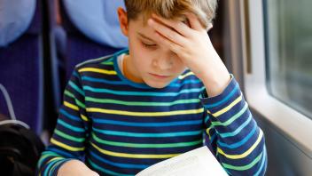 Young boy reading book with hand on his forehead