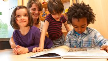 Elementary teacher with three of her students looking at a picture book
