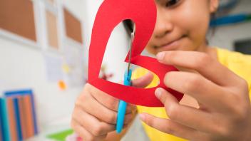 Child cutting heart out of red paper