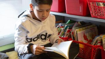 elementary school student sitting near classroom library bins and reading