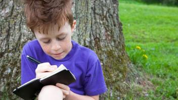 Red-headed young boy outside writing in notebook